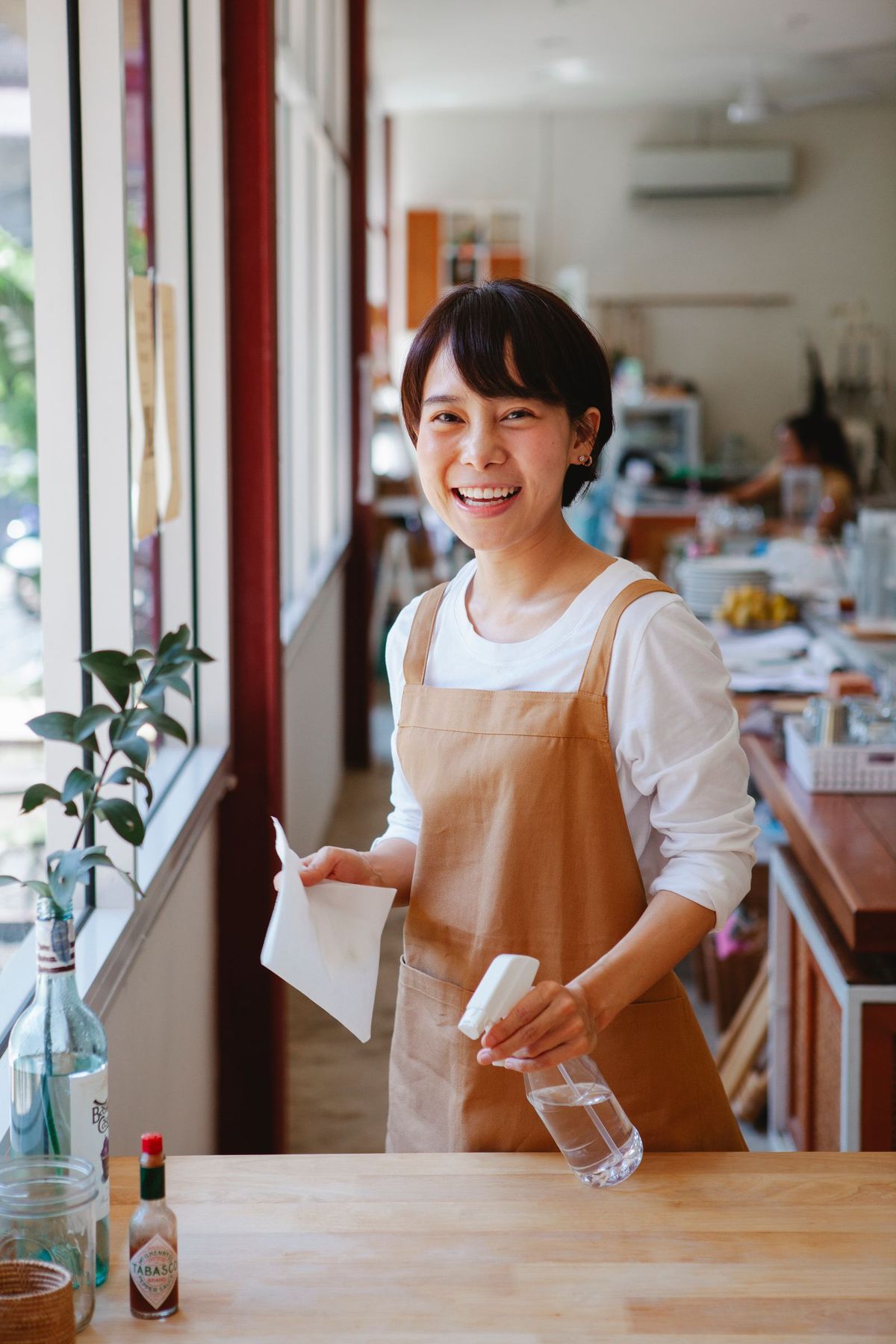 Smiling young CleanKaki cleaner in an apron holding a cleaning cloth