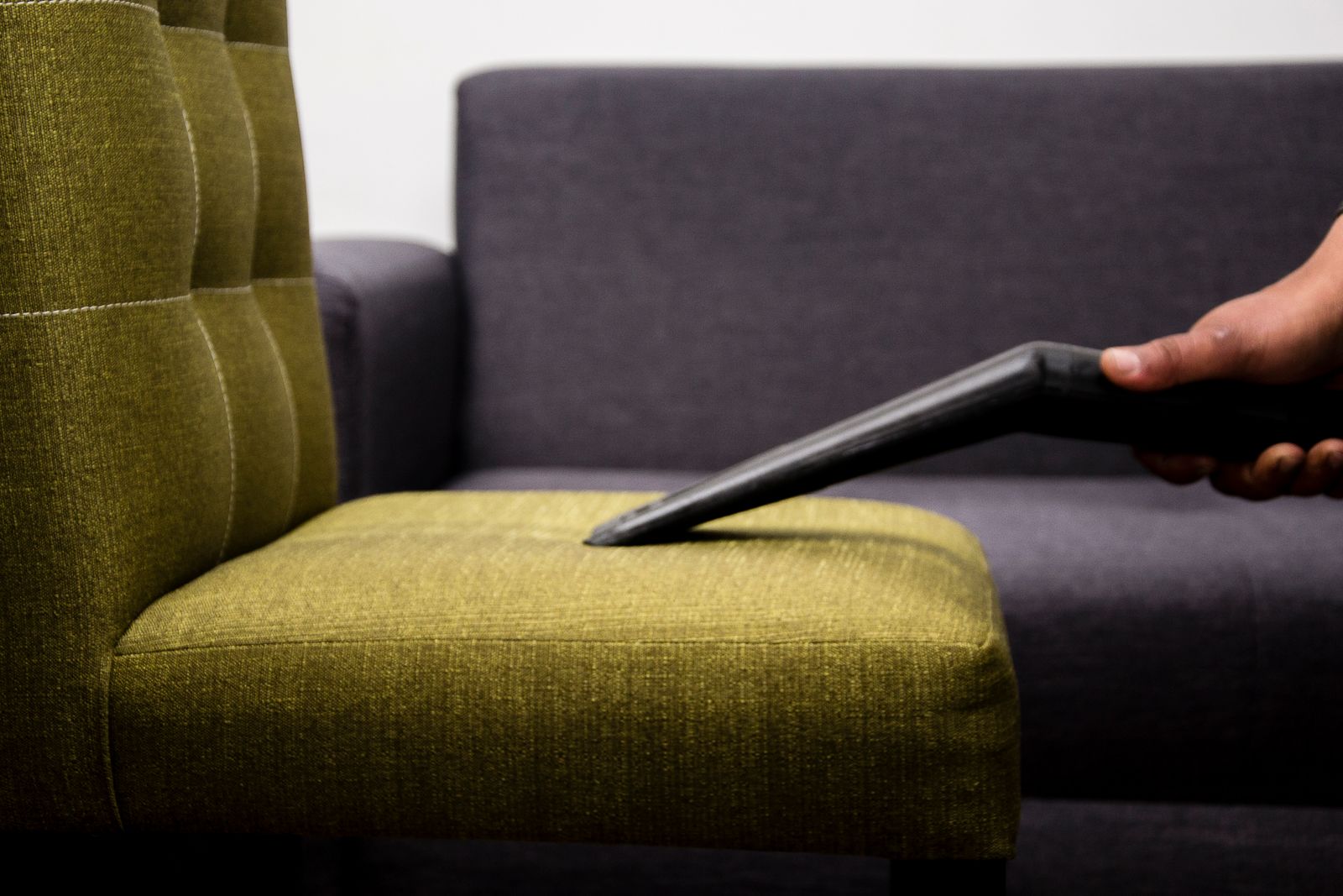 Vacuuming a green fabric sofa during upholstery cleaning